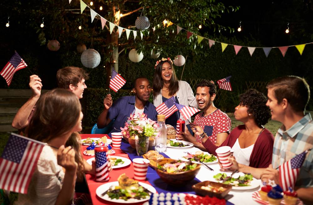 a group of friends celebrating 4th of July in the backyard iwth flags and food