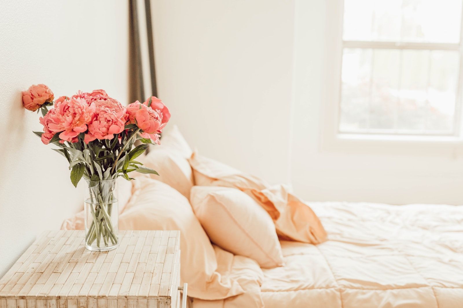 chambre à coucher lumineuse et romantique avec une literie pêche et des fleurs dans un vase sur la table de chevet