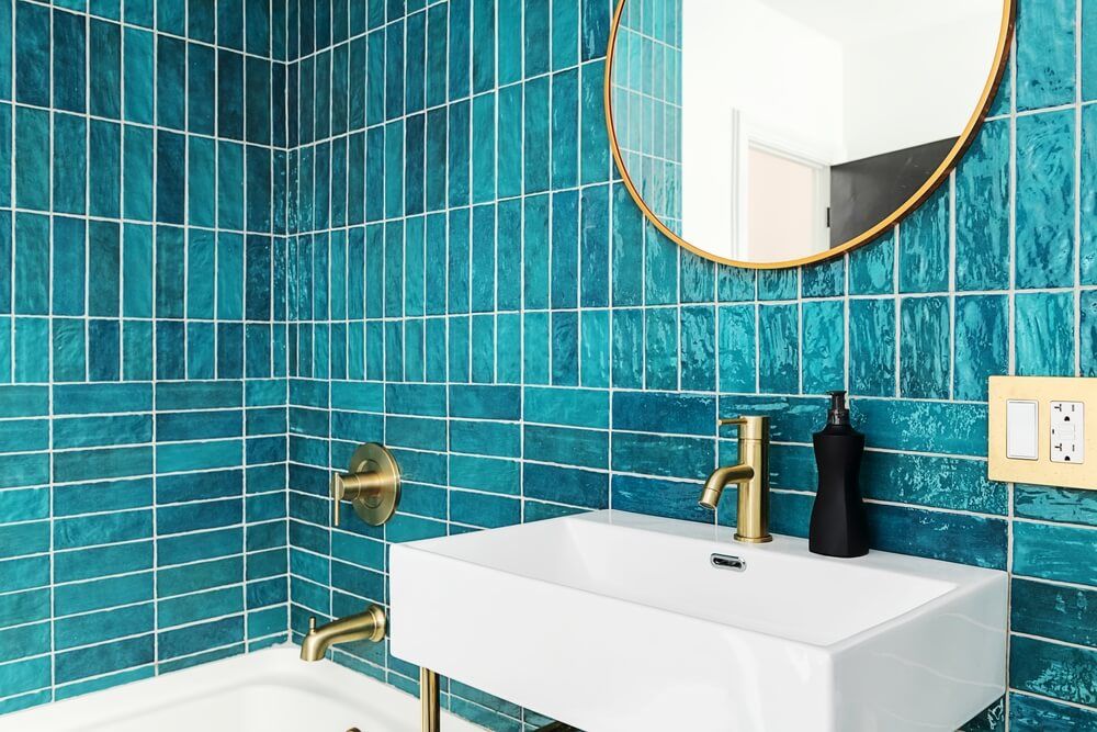 Modern and Vibrant Bathroom. Blue and Green Tile bathroom with gold fixtures and mirror.