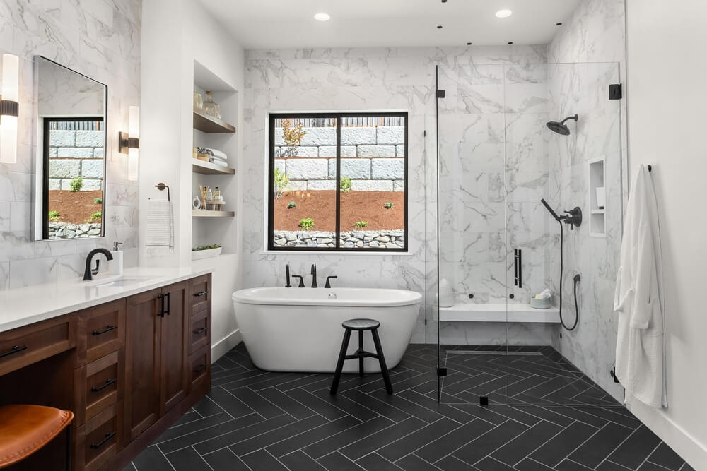 Beautiful bathroom in luxury home with double vanity, bathtub, and shower. Features herringbone tile on floor and marble tile on wall and backsplash.