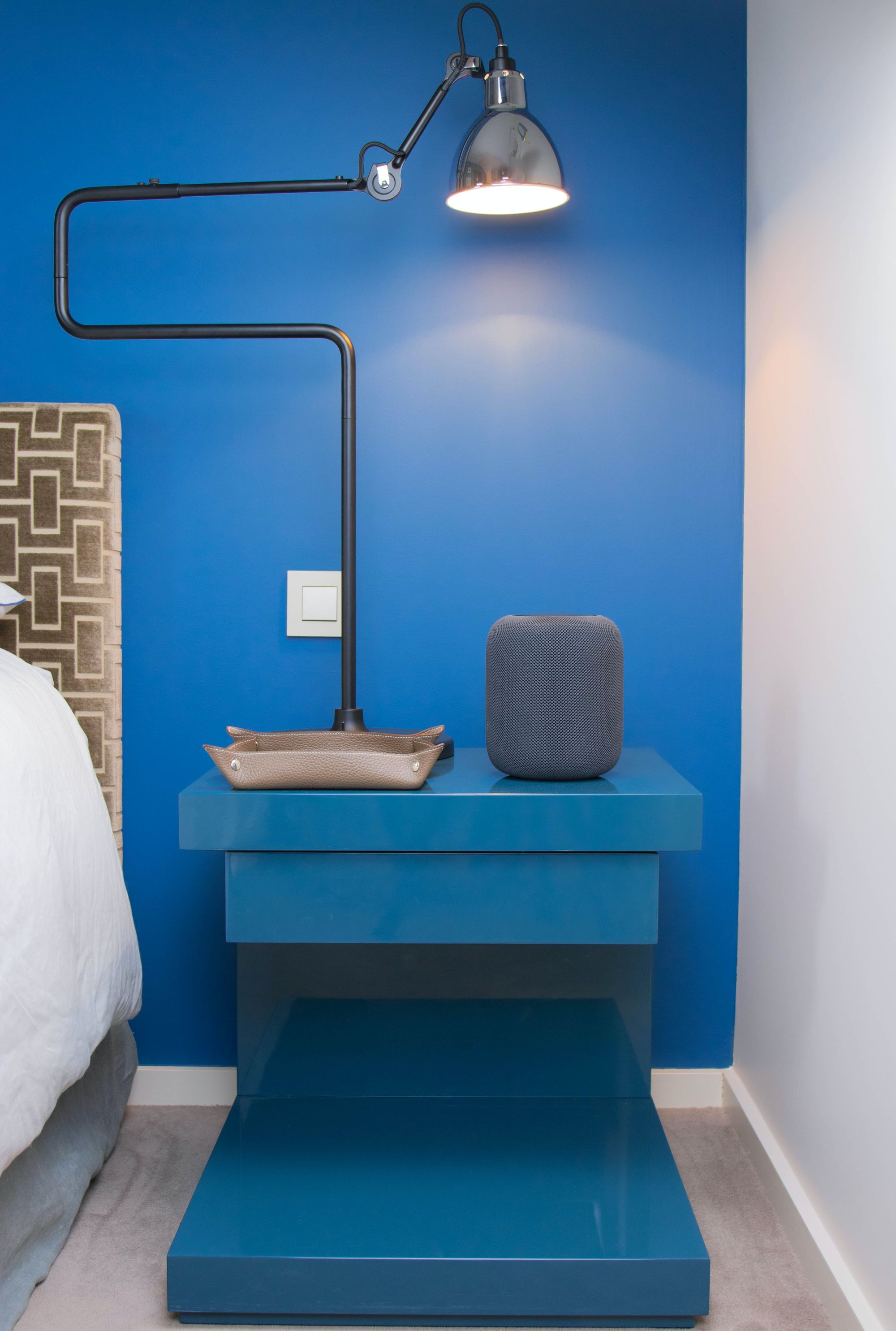 dormitorio con mesita de noche y pared azul, bandeja de piel, alexa y lámpara