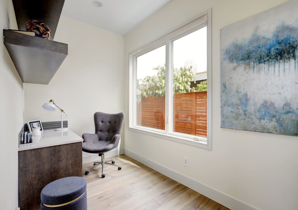 Light small home office interior with corner desk and grey upholstered chair on hardwood floor