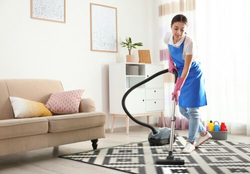 une femme de ménage passant l'aspirateur sur un tapis à carreaux dans un salon