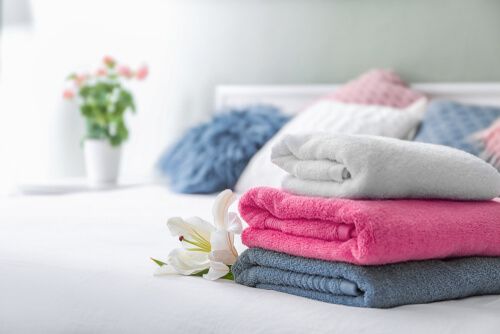 folded towels of different colors piled up on a bed, with a flower
