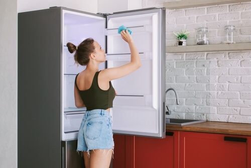 fille nettoyant le réfrigérateur en short