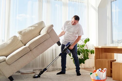 a man lifting up a sofa to hoover the carpets