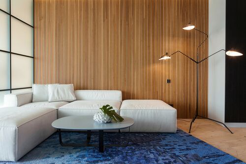 cream sofa in fron of wooden wall with a blue carpet, an oval coffee table, and a standing lamp