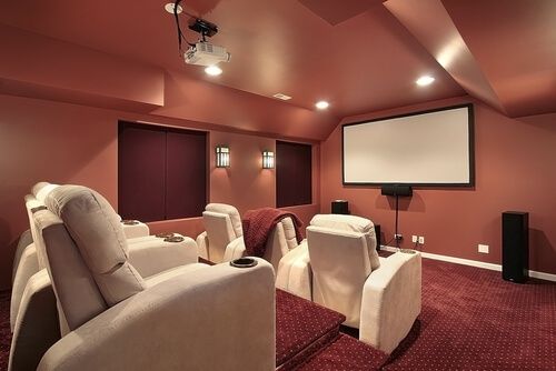 домашний кинотеатр с проектором, мягкими креслами и закрытыми окнами в красных тонах