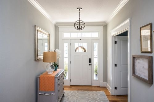 A wide front foyer with transom, hanging light fixture, coastal colors and entry way table
