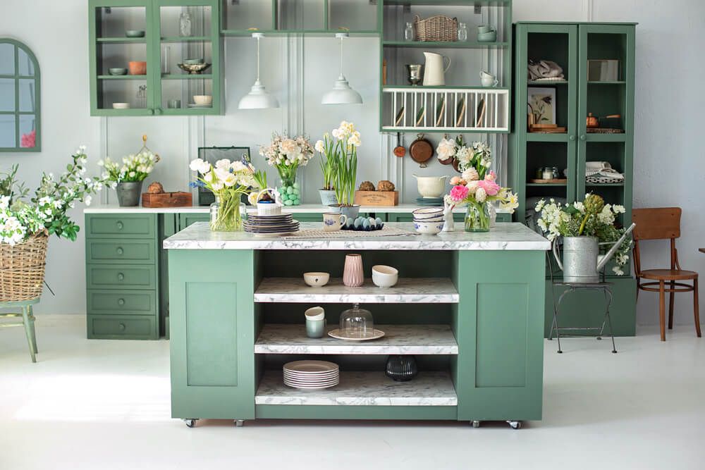 Une cuisine verte dans un décor printanier. Ustensiles de cuisine, vaisselle et assiette sur la table de l'îlot de cuisine.