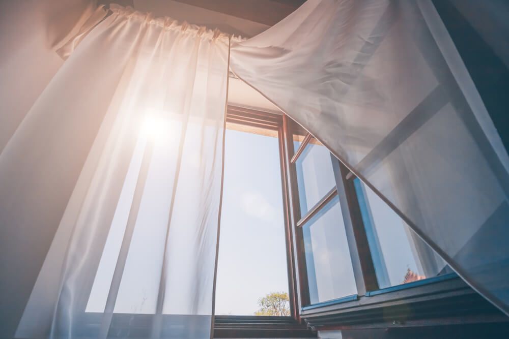 Morning sunshine peeking through an open window and sheer curtains