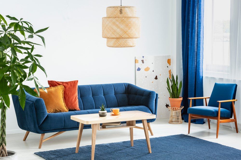 Wohnzimmer mit blauen Möbeln und blauem Teppich, mit Pflanzen und bunten Kissen