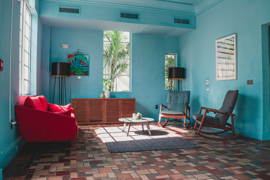 sala de estar en colores en contraste, sillas de madera, paredes azules y sofá rojo 