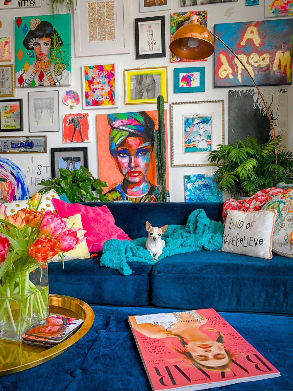 intérieur maximaliste avec un canapé en velours bleu foncé, de nombreux tableaux au mur et un chihuahua reposant sur le canapé  