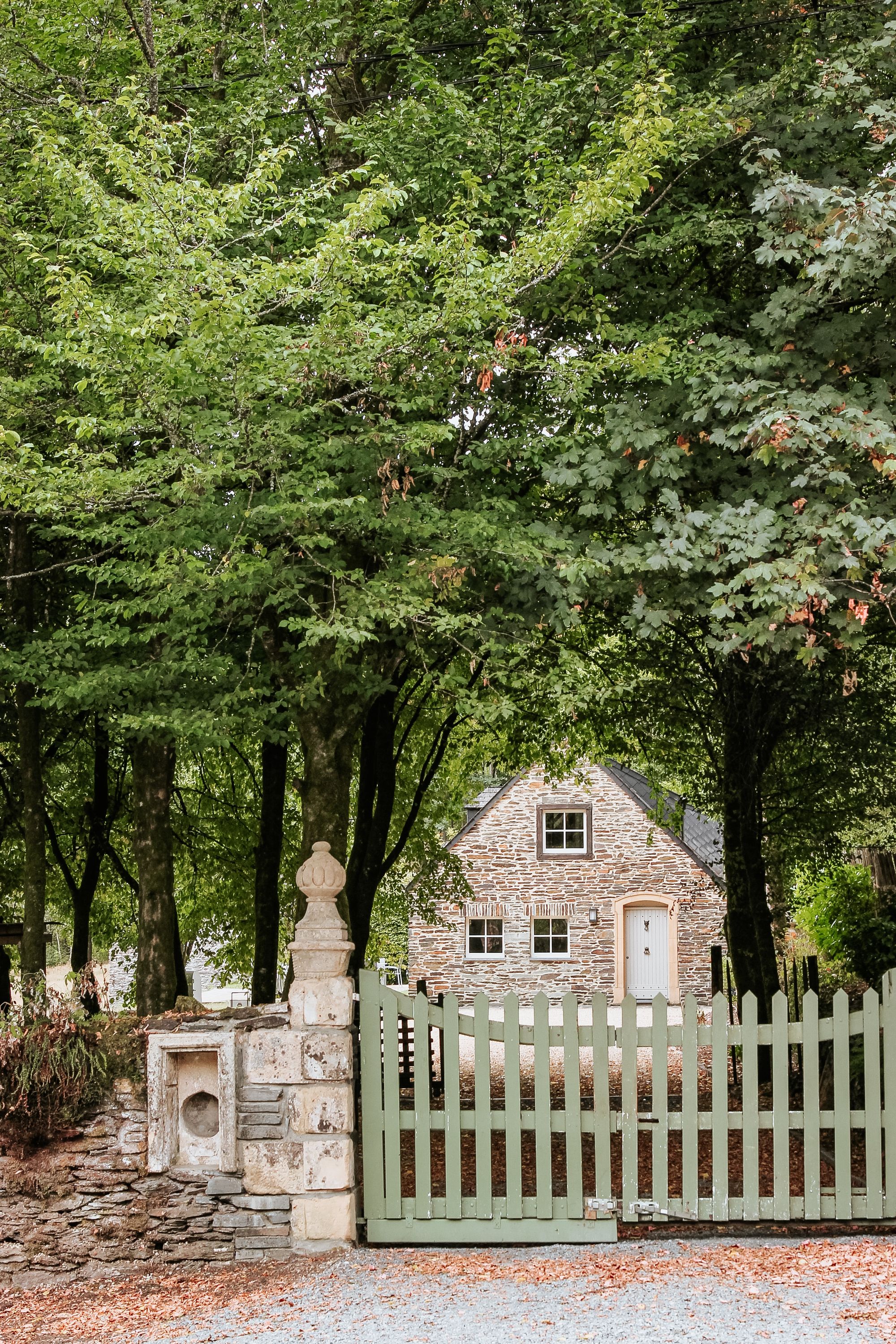 fachada de casa de piedra con verja de piedra y portón de madera verde sage