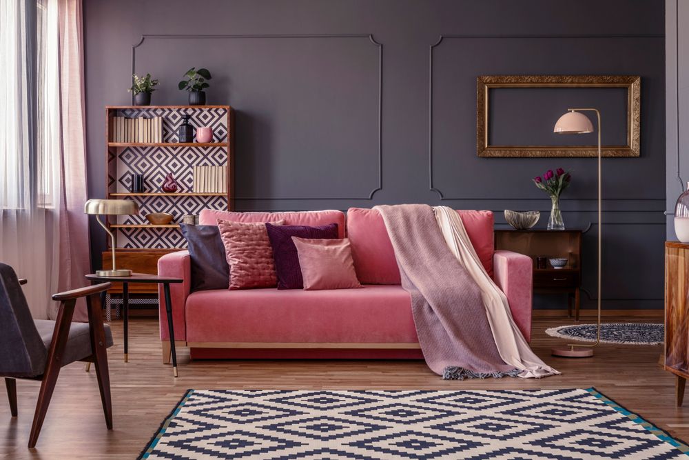 Pastel pink blanket on a matching sofa in living room with elegant, golden frame on a dark grey wall