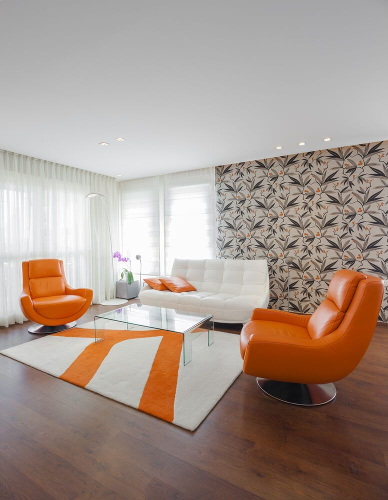 salon avec des fauteuils rétro orange vif et un mur d'accent avec du papier peint à motifs