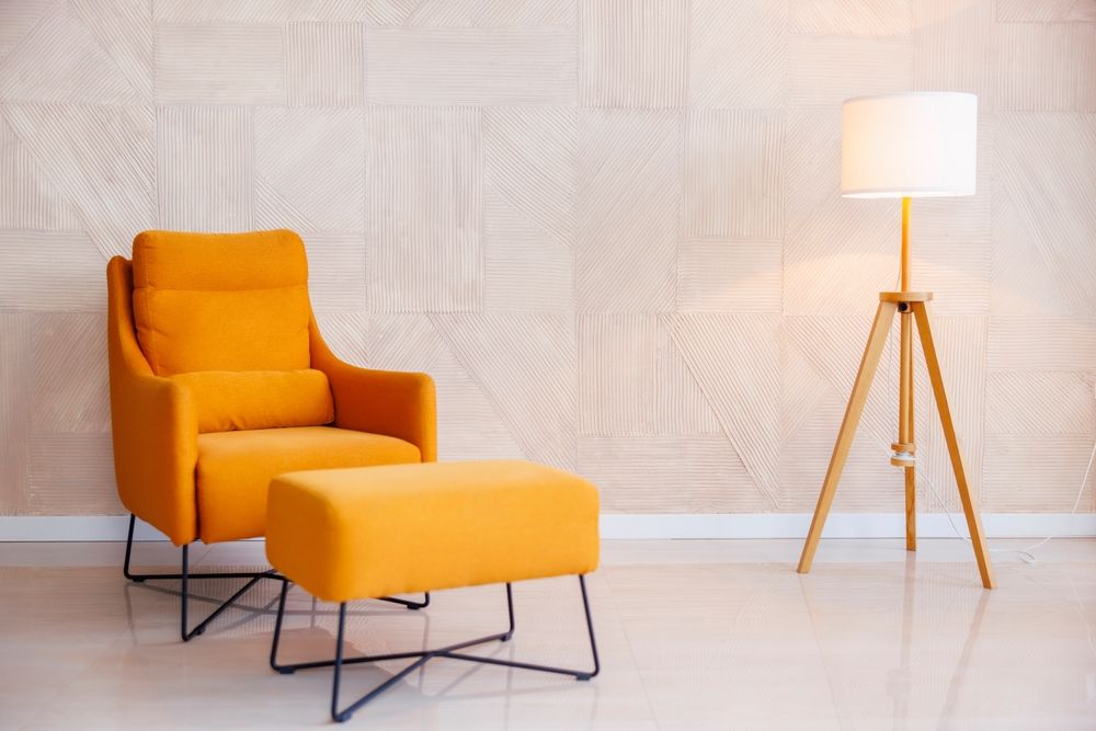 ein orangefarbener Sessel und Fußstütze und eine Stehlampe vor einer blassrosa Wand 