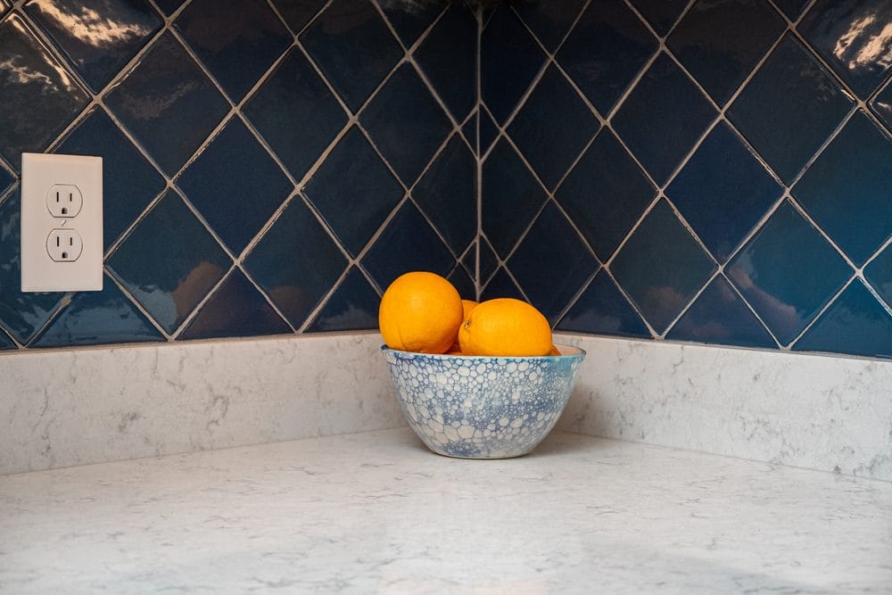 Oranges in a blue and white bowl on a granite counter with a blue tile backsplash