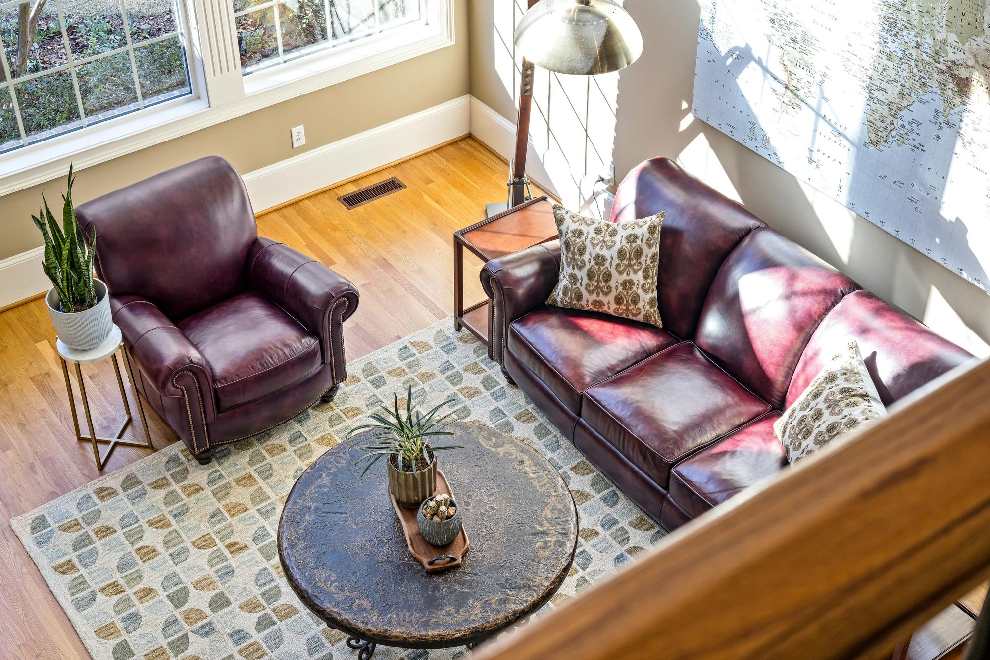 Vista superior de um aconchegante mezanino com piso de madeira, mobiliado com sofá e poltrona de couro vinho, uma mesa de centro redonda rústica, e plantas decorativas. Foto: Curtis Adams no Pexels