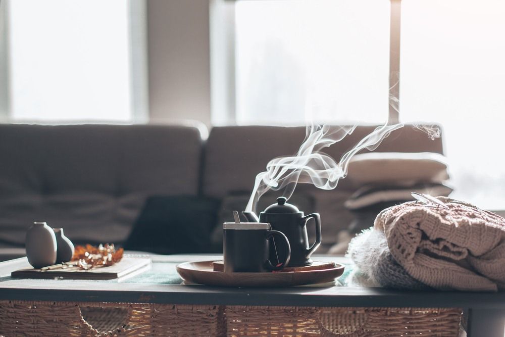 Sweaters and cup of tea with steam on a serving tray on a coffee table.