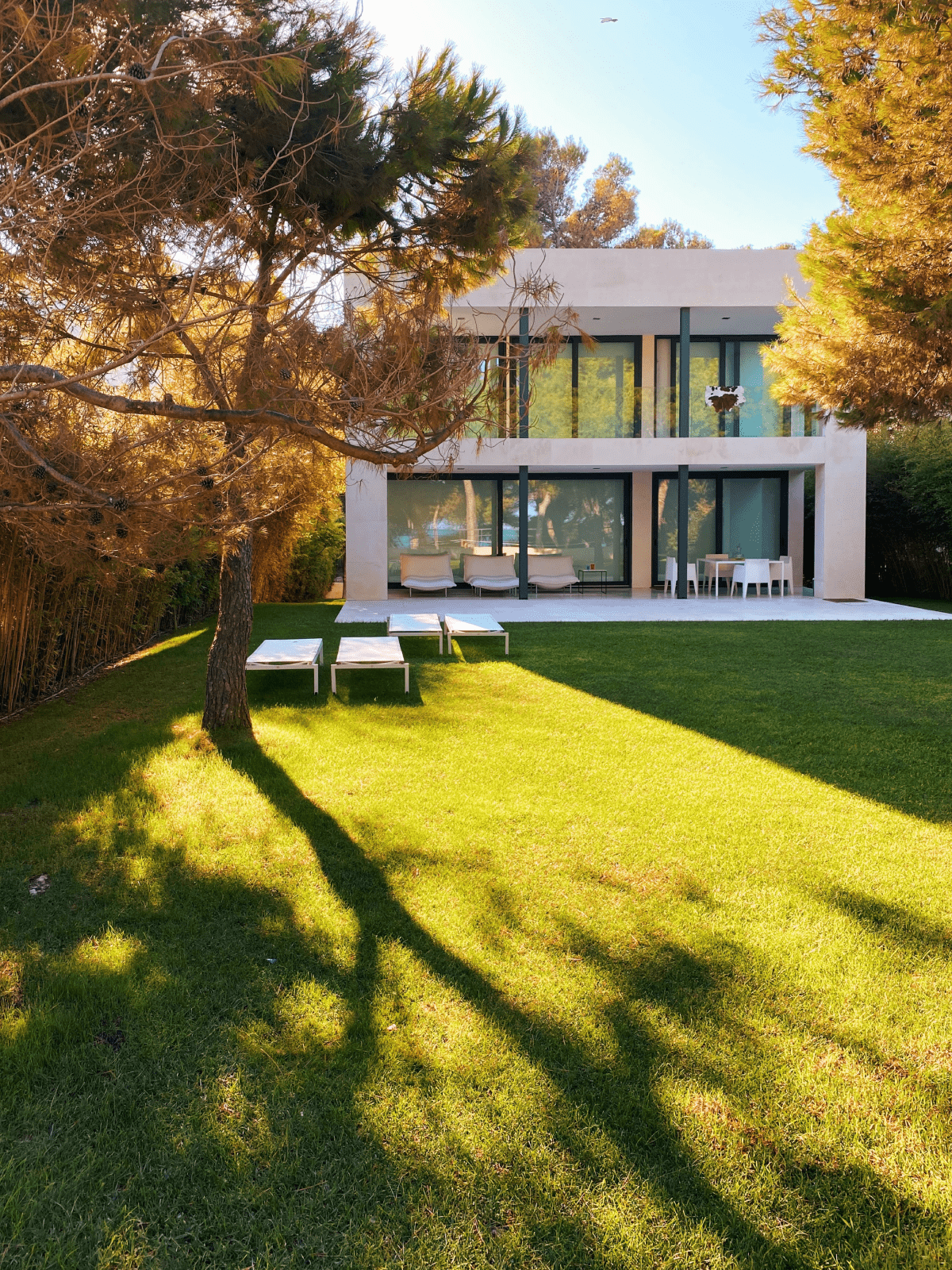 casa de campo moderna de dos pisos con cristalera y jardín con césped y árboles