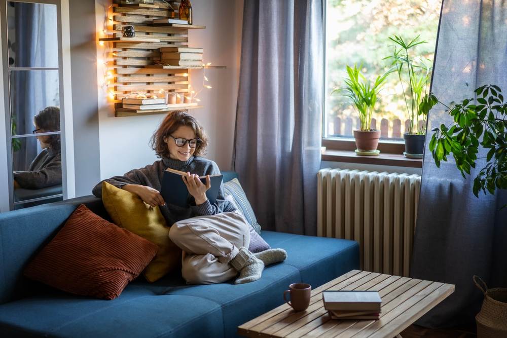 woman in a warm sweater reading a book while sitting on the couch