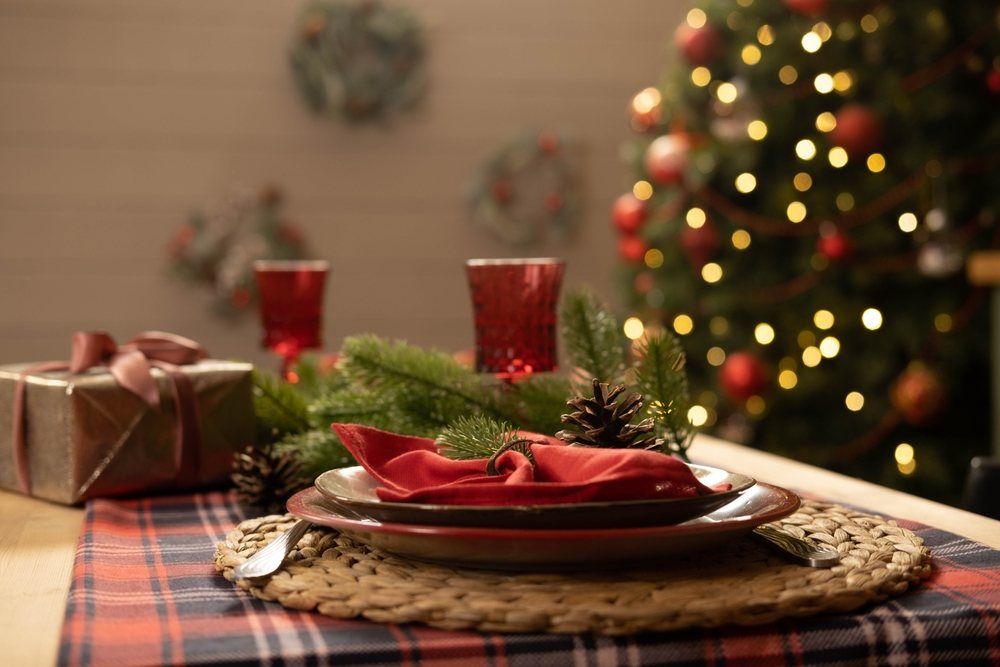 Table de Noël décorée d'une serviette rouge, d'une nappe à carreaux rouges et d'une pomme de pin