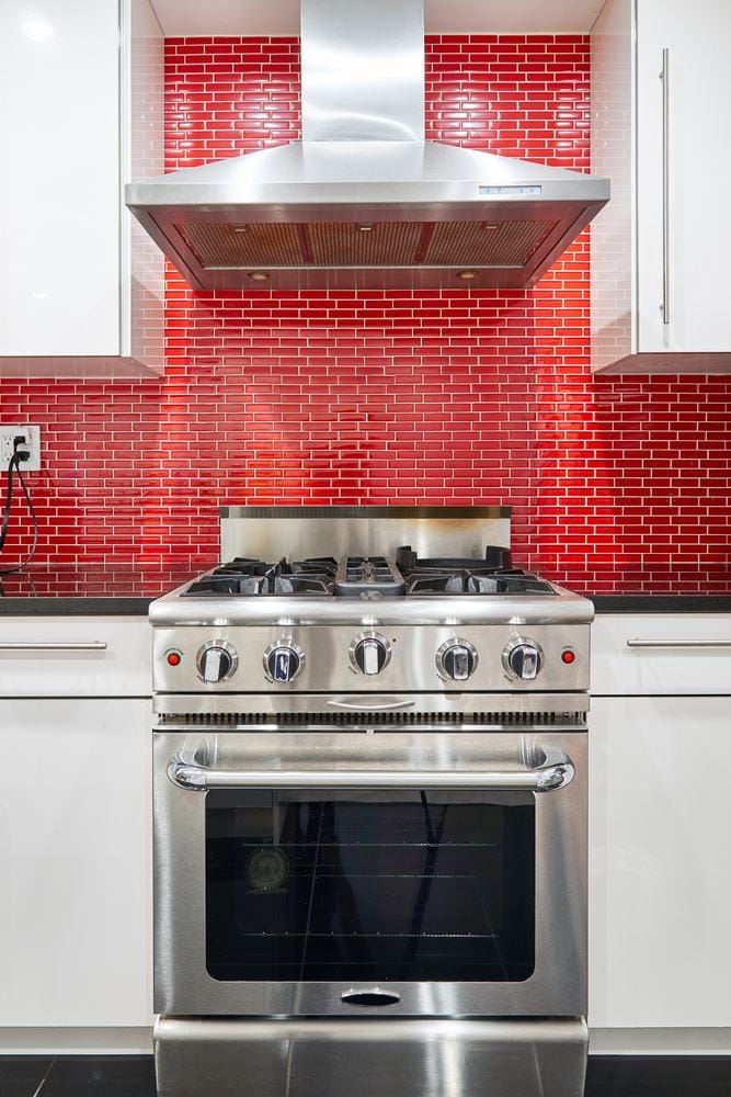 Modern kitchen with white cabinets, red back splash, stainless steel range oven and hood.