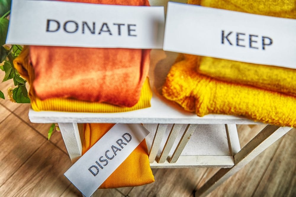 Signs with the words keep, donate, discard and fashion clothes folded in stacks in cozy room