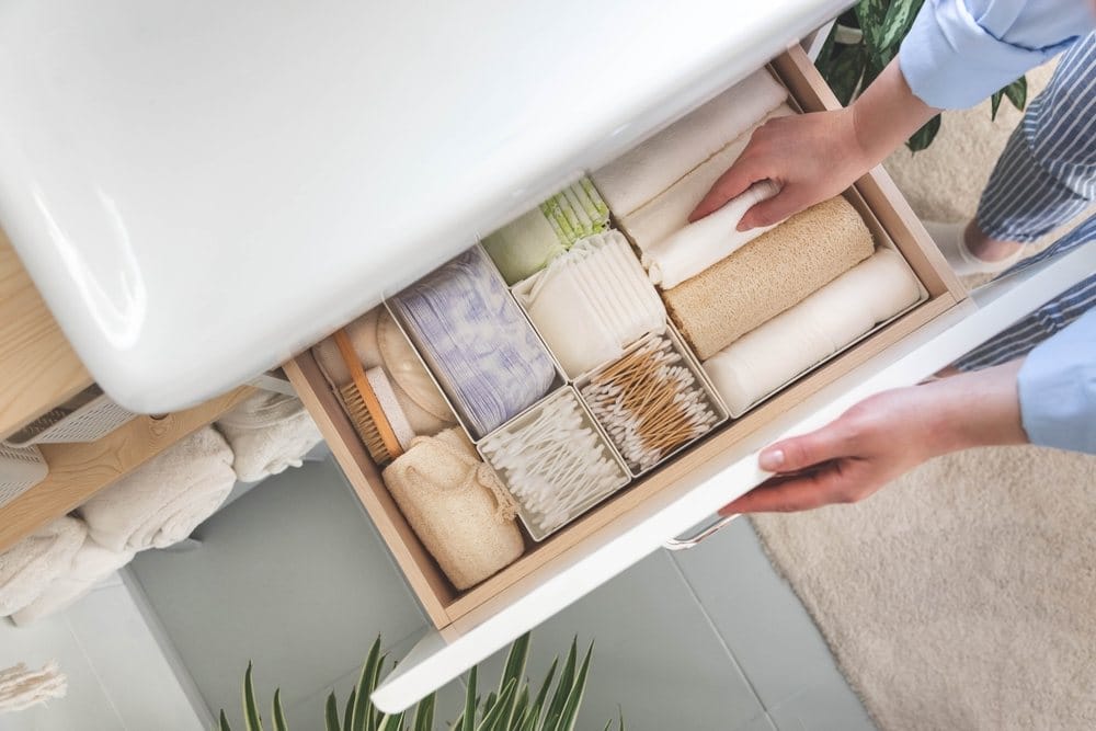 Top view of woman hands neatly organizing bathroom amenities and toiletries in drawer or cupboard in bathroom.