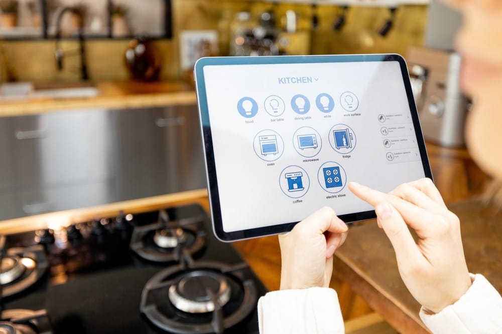 Woman holding digital tablet with running smart home application, controlling kitchen devices remotely.