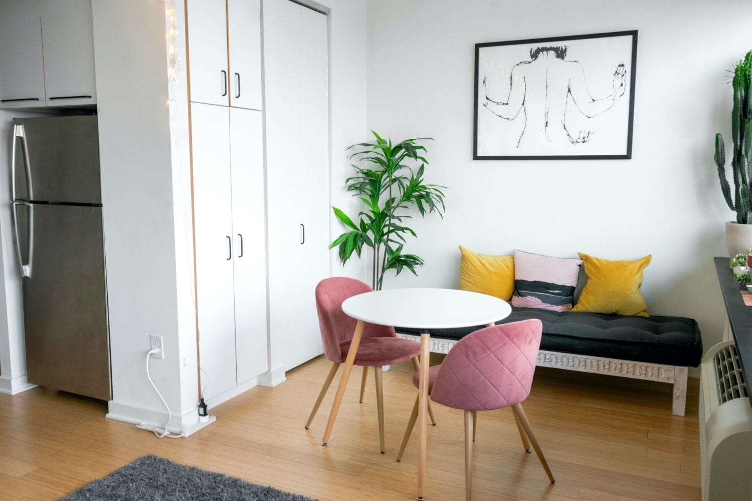 kleiner Raum mit einem schmalen runden Tisch, rosa Stühlen, einem kleinen Sofa und bunten Kissen
