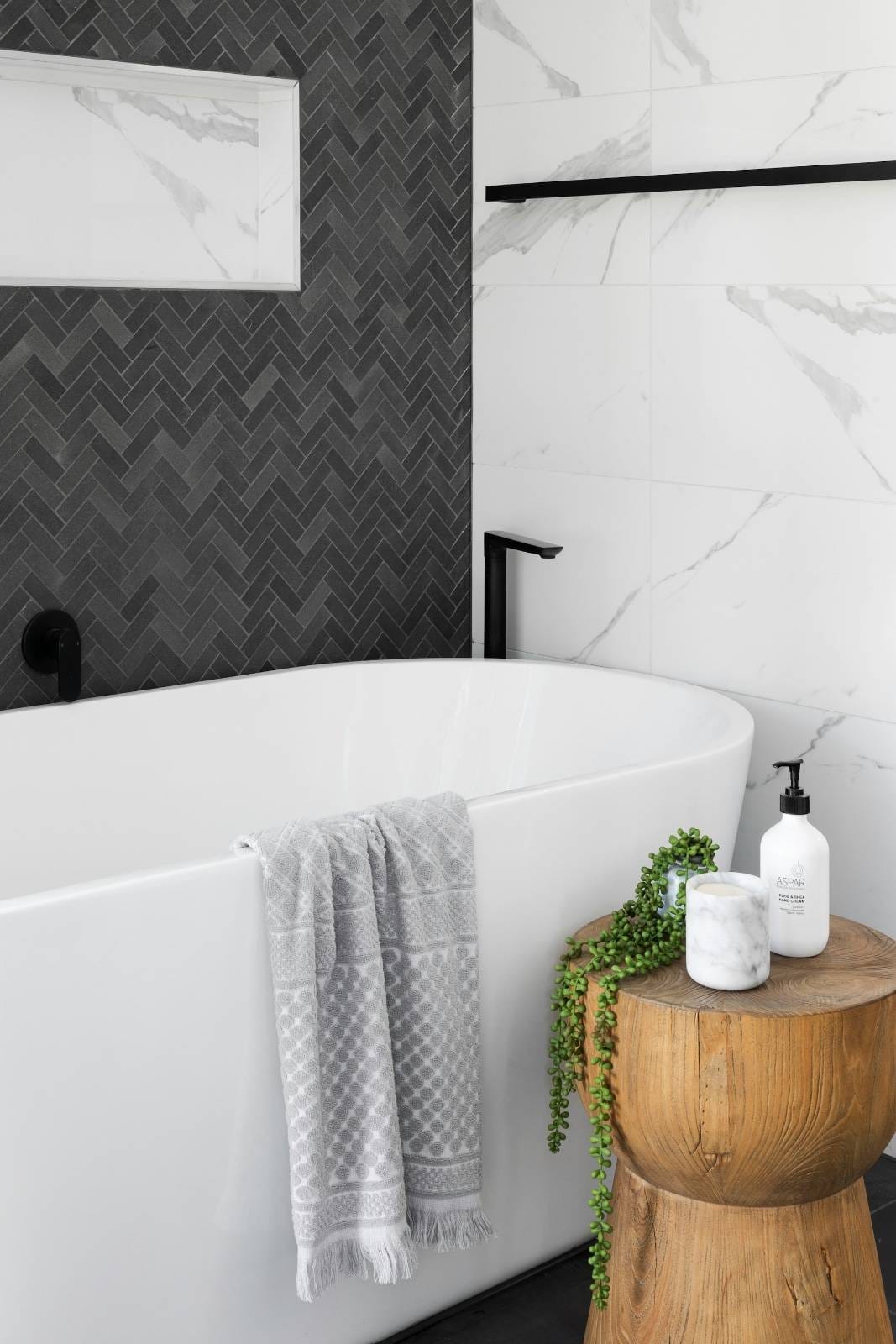 eine Badewanne und eine Badezimmerwand mit grauen und marmorweißen Fliesen