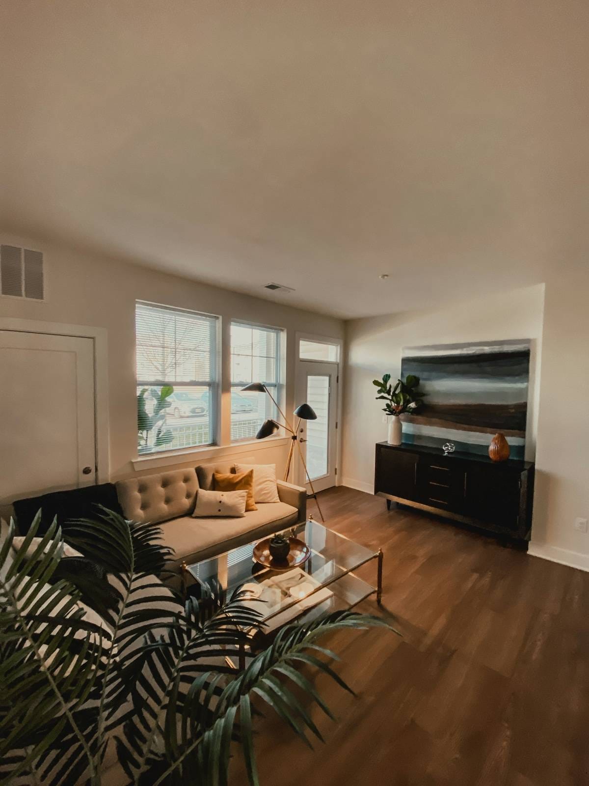 Minimalistisches Wohnzimmer mit einem Couchtisch aus Glas, einem Fernseher, Pflanzen und einem schwarz-weißen Sofa