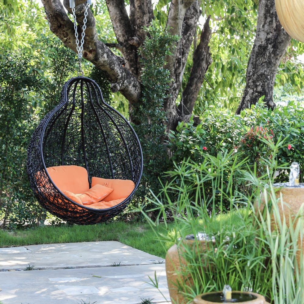 un fauteuil suspendu avec des coussins orange dans un jardin