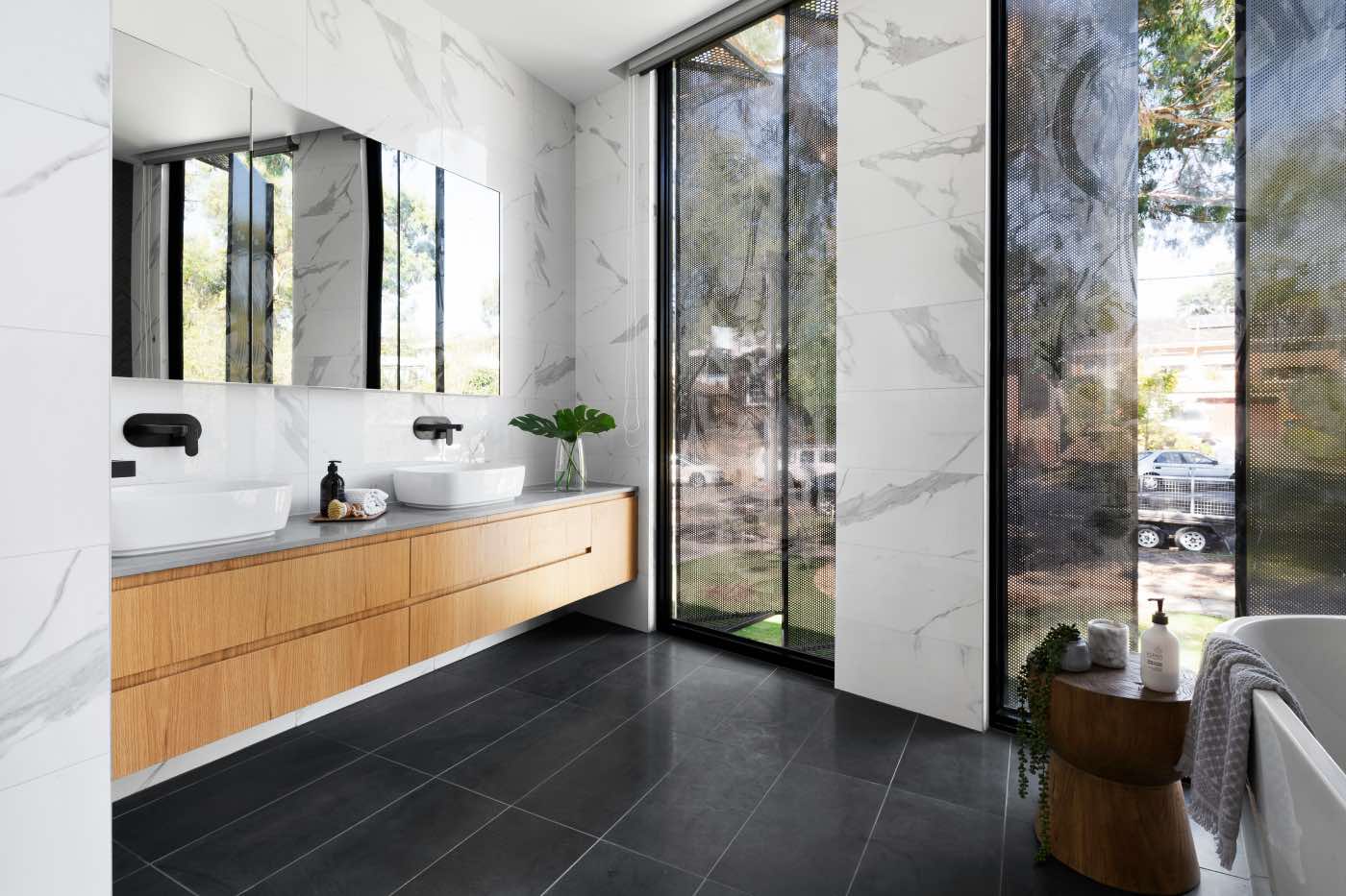 big modern renovated bathroom with white marble walls and wood cabinetry
