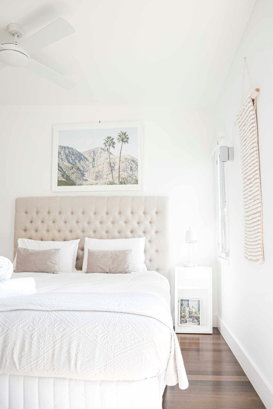 un coin de chambre apaisant avec une literie blanche, une photo de palmiers et une moquette rose pâle