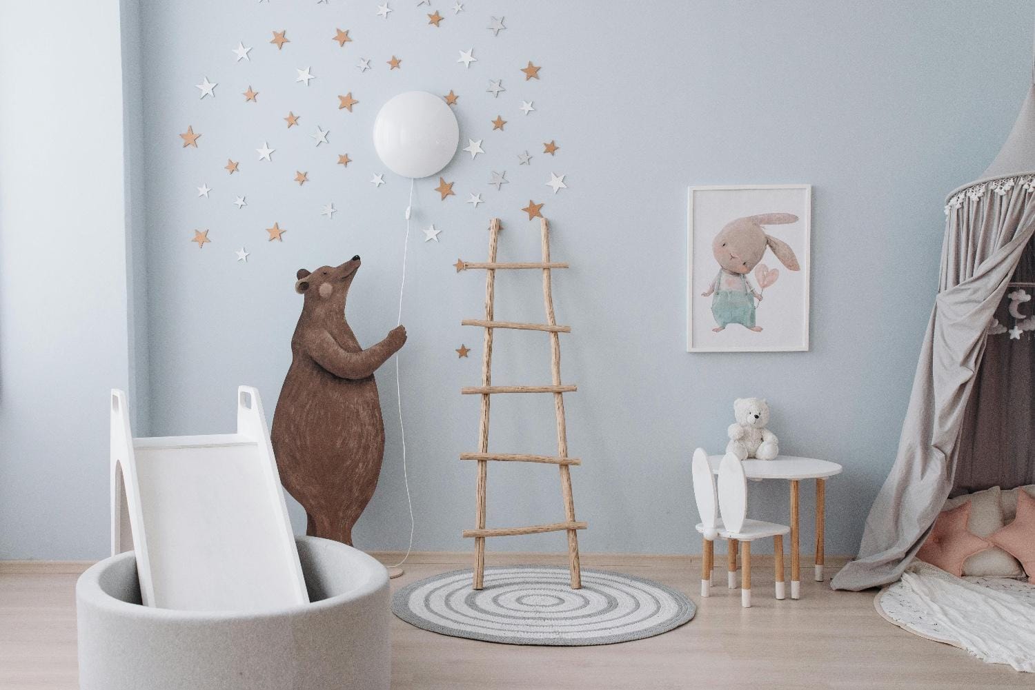 ein Kinderzimmer mit hellblauen Wänden, einem Bild von einem Hasen und einem Bären als Wandsticker