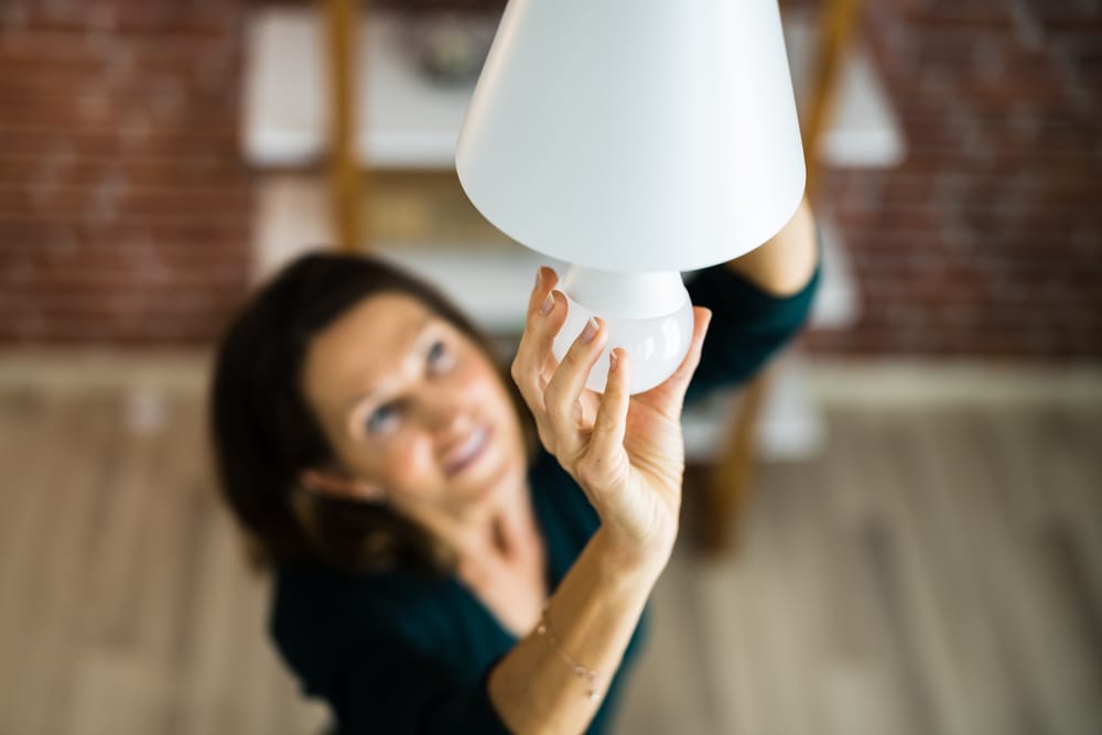 eine Frau dreht eine LED-Glühbirne in einer weißen Lampe ein