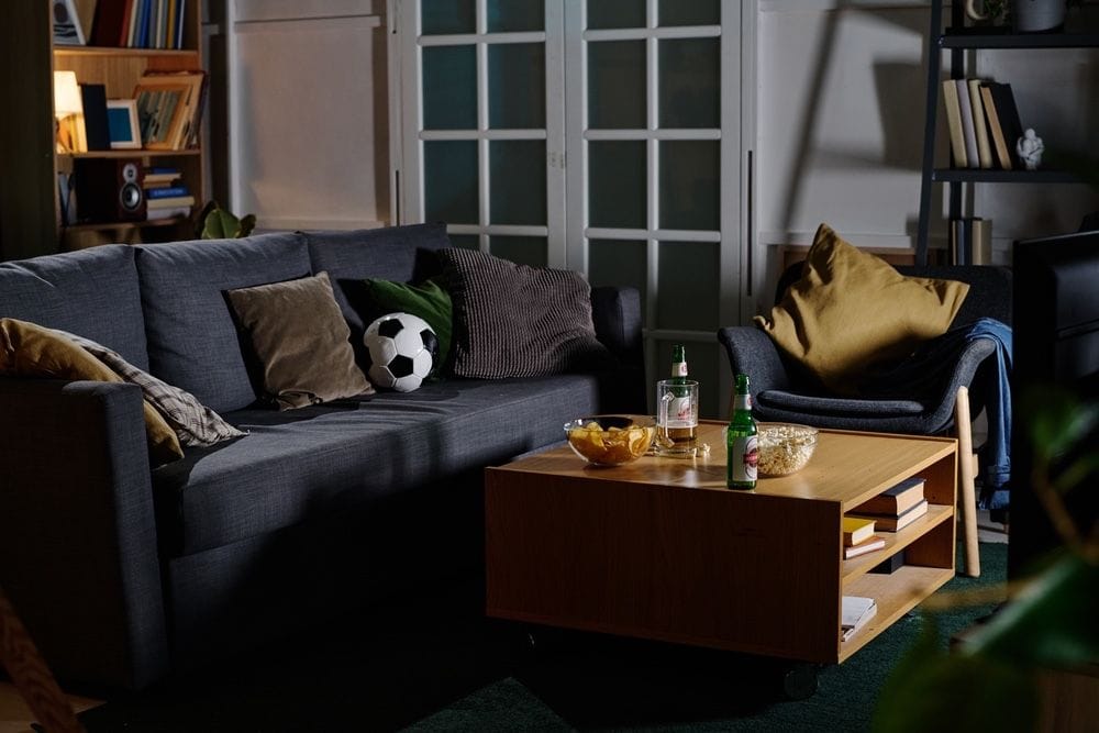 eine Couch in einem Wohnzimmer mit einem Fußball, Snacks und Bier auf dem Tisch