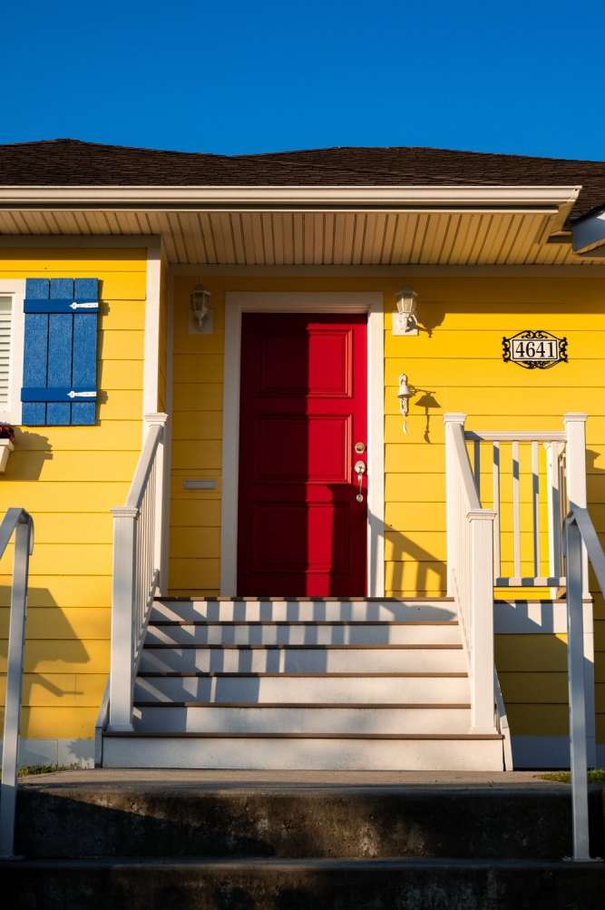 Casa simples amarela com escada branca e porta vermelha