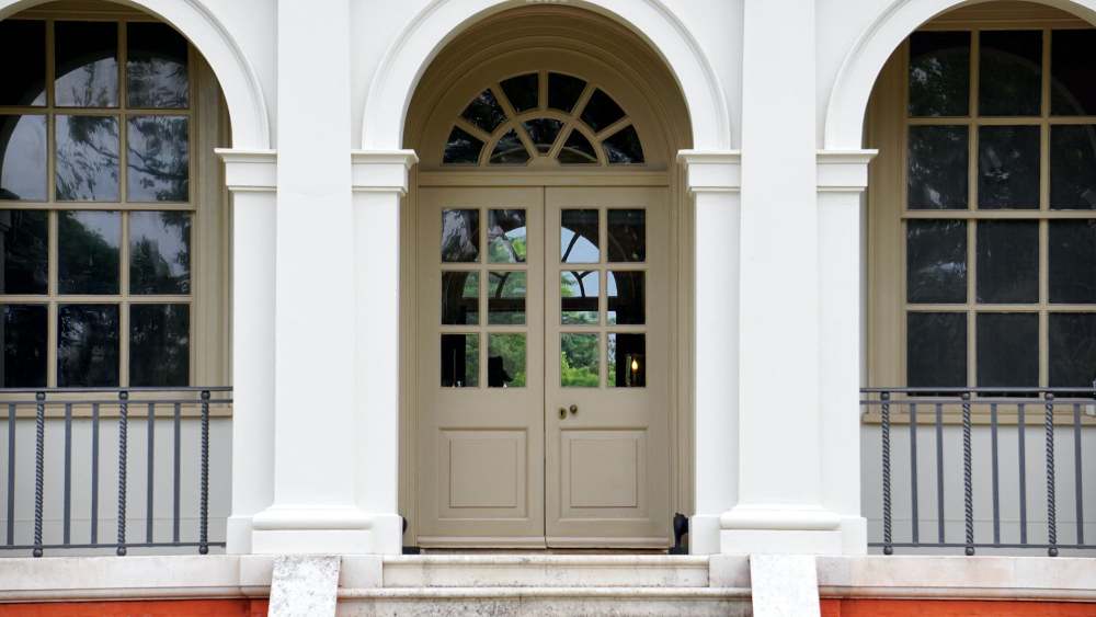 Frente de casa simples com porta de madeira pintada de bege claro e vidro