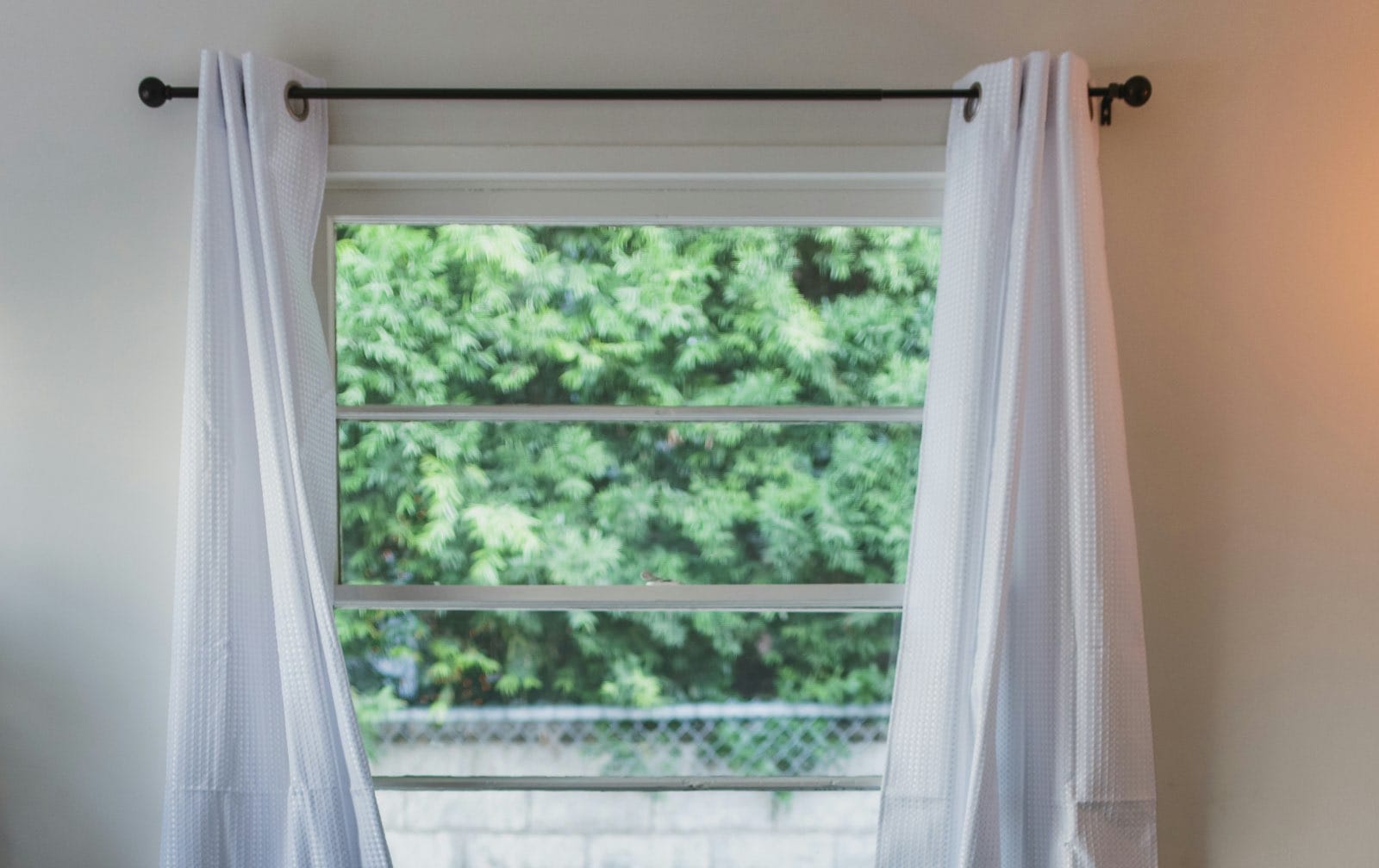 ventana con cortinas con ollaos blancas con barra de cortinas negra