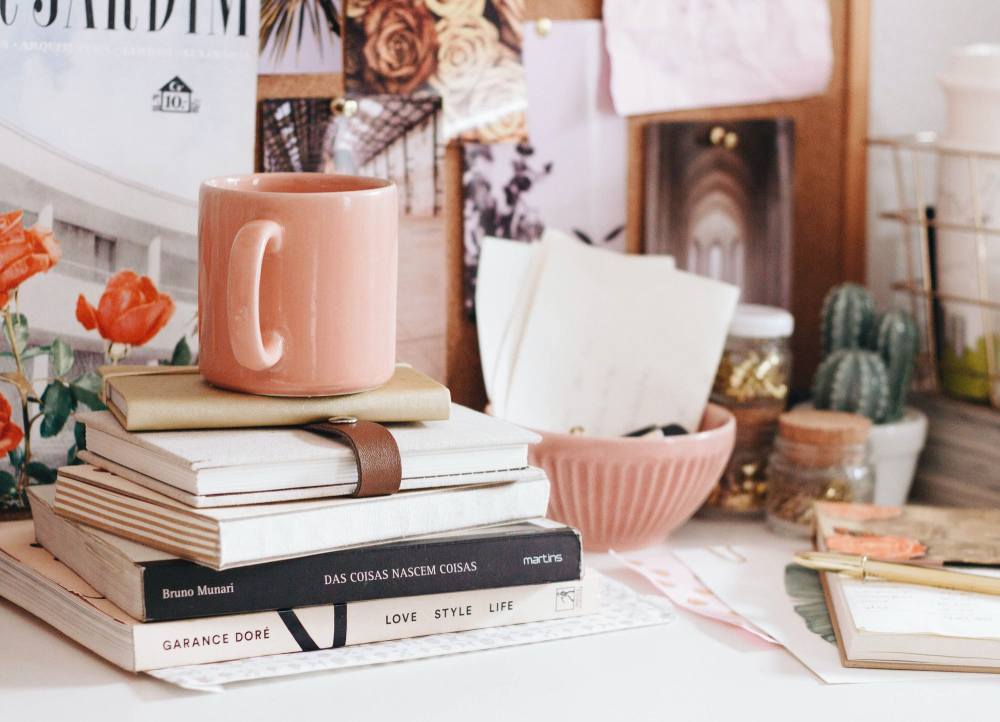 mesa com decorada com livros e tons de rosa na xícara e no pote