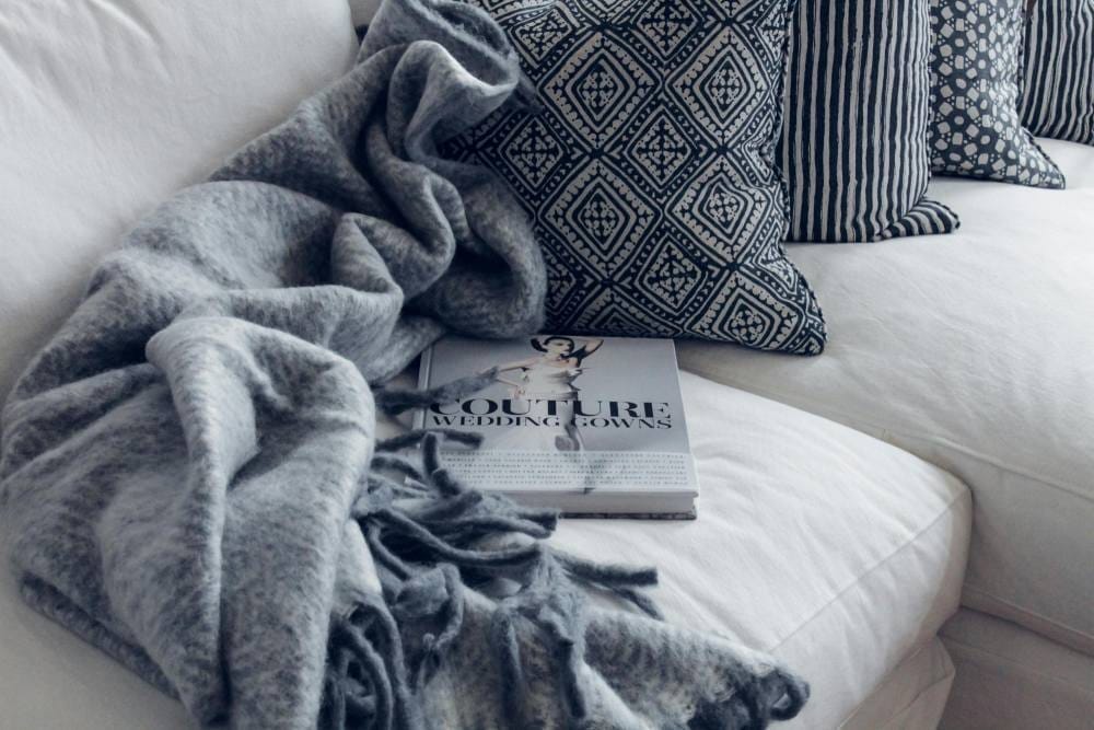 sofá branco decorado com manta e almofadas tom de cinza