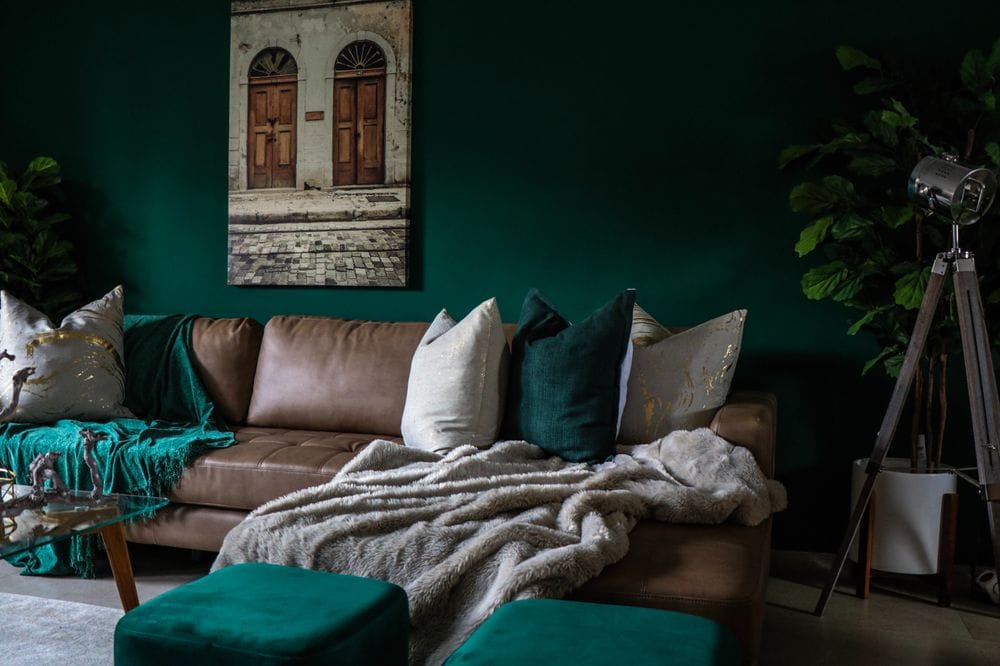 Quarto verde com sofá de couro marrom decorado com almofadas de cores diferentes porém seguindo a mesma paleta de cores do quarto