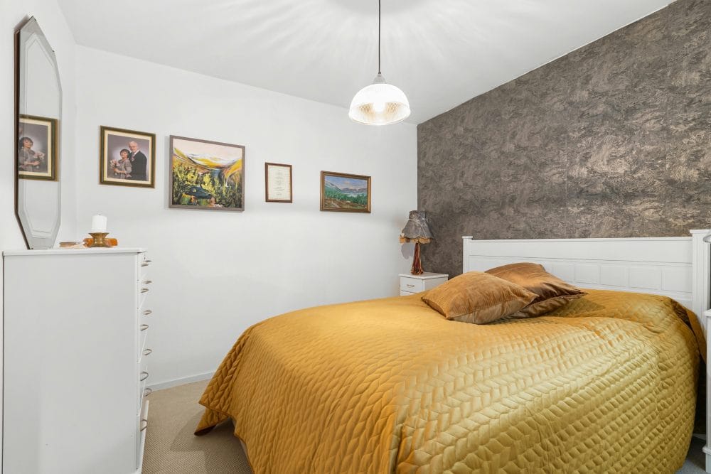 Quarto de casal decorado com manta amarela mostarda e quadros na parede