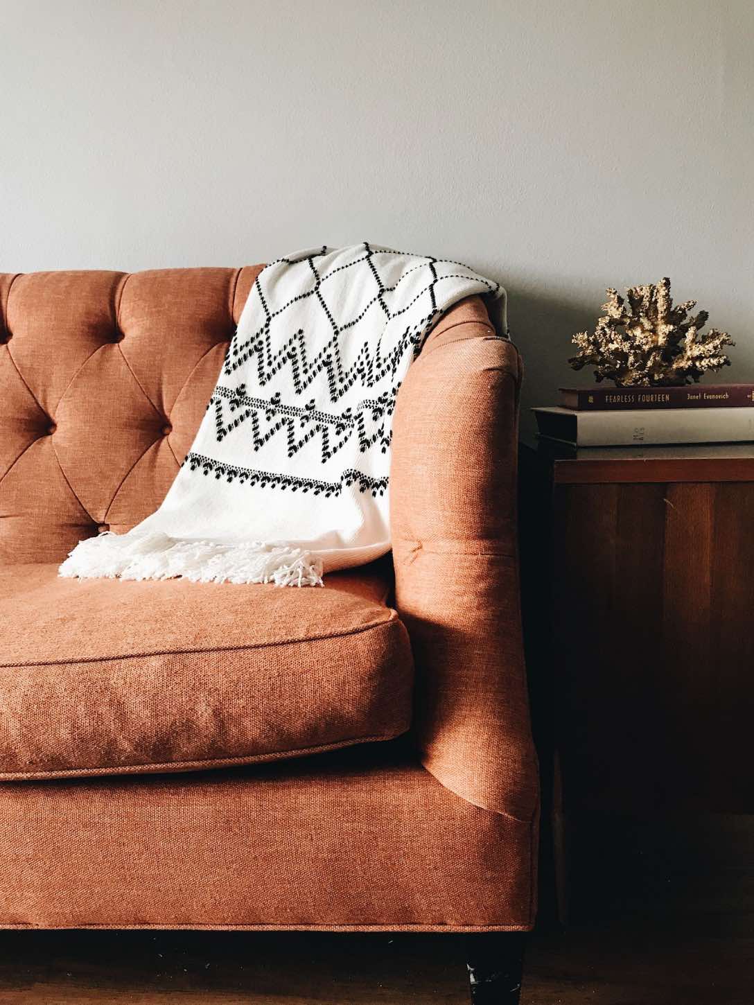 decoración otoñal con sofá de tela naranja y manta blanca y negra