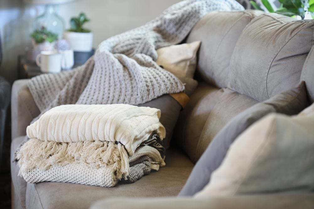 Stack of a variety of soft knit throw blankets stacked on a grey couch